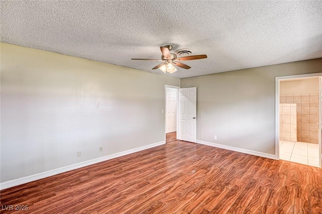 unfurnished bedroom featuring visible vents, wood finished floors, baseboards, connected bathroom, and a textured ceiling