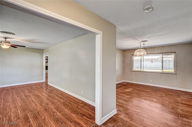 unfurnished room with a textured ceiling, visible vents, wood finished floors, and ceiling fan with notable chandelier