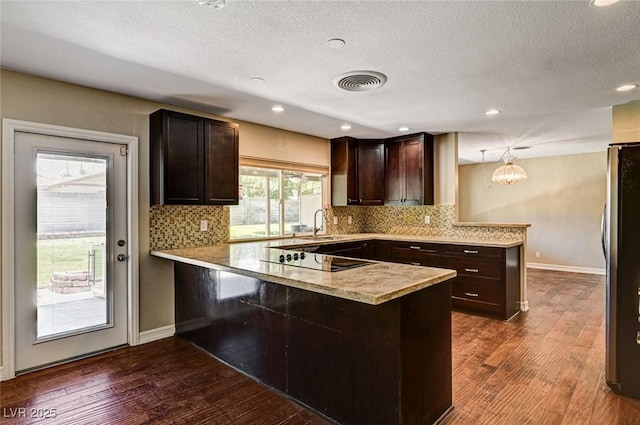 kitchen featuring freestanding refrigerator, a peninsula, dark brown cabinets, black electric stovetop, and light countertops