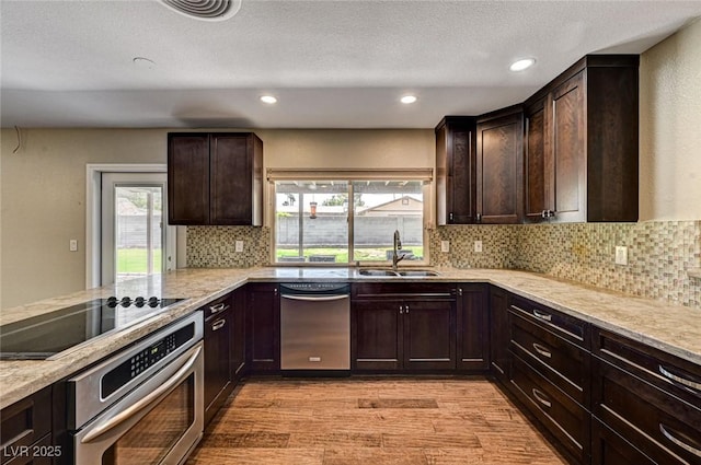 kitchen with dark brown cabinetry, appliances with stainless steel finishes, a sink, and light wood finished floors