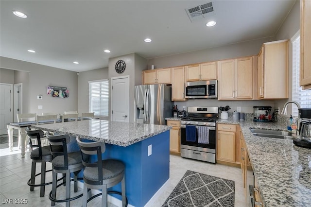kitchen featuring a breakfast bar, a sink, light brown cabinets, stainless steel appliances, and visible vents