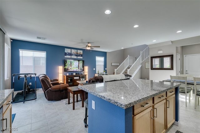 kitchen with visible vents, a kitchen island, ceiling fan, light stone counters, and light tile patterned floors