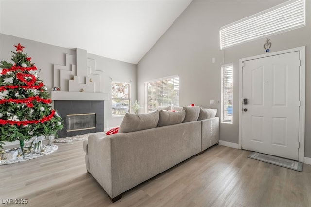 living area featuring high vaulted ceiling, a tiled fireplace, baseboards, and light wood-type flooring