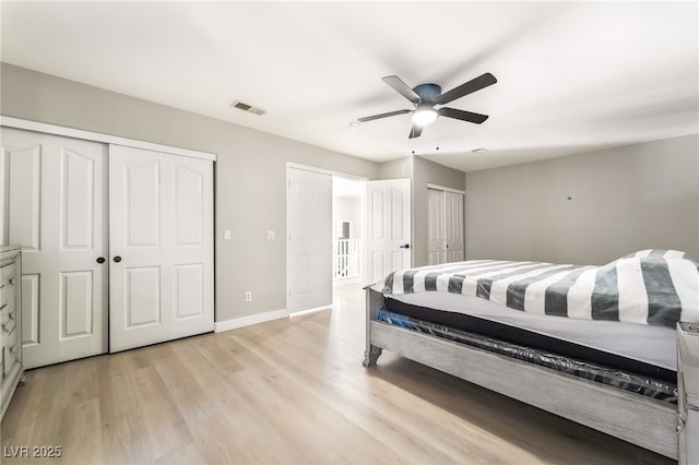 bedroom featuring visible vents, two closets, baseboards, a ceiling fan, and light wood finished floors