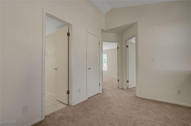 interior space with baseboards, vaulted ceiling, and light carpet