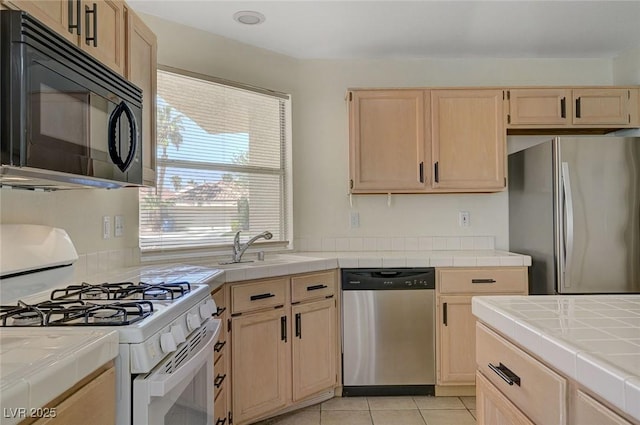 kitchen with a sink, light brown cabinets, tile counters, and stainless steel appliances