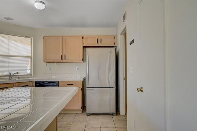 kitchen with freestanding refrigerator, light brown cabinets, tile countertops, a sink, and light tile patterned floors