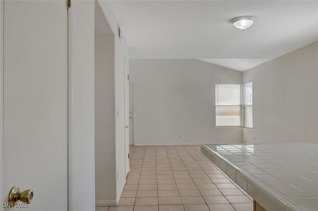 empty room featuring light tile patterned floors, baseboards, and vaulted ceiling