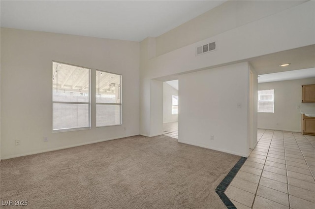 unfurnished room with visible vents, light tile patterned floors, a healthy amount of sunlight, and light carpet