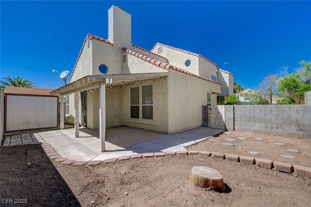 back of property featuring a tiled roof, a chimney, a fenced backyard, a patio, and stucco siding