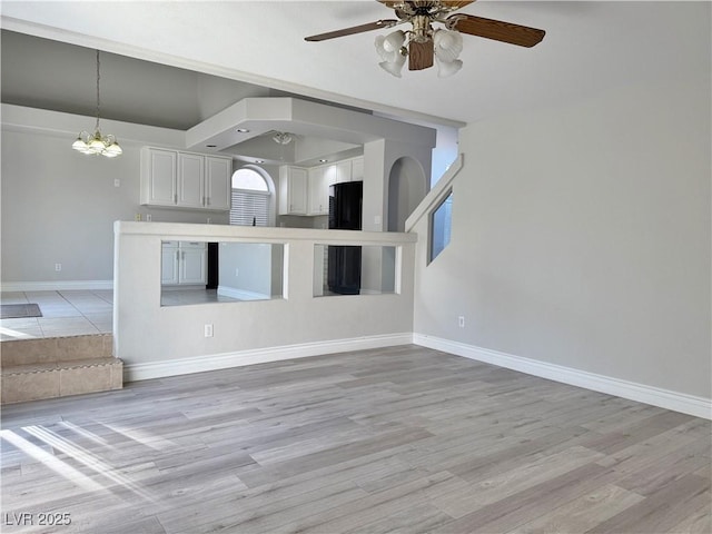 unfurnished living room featuring baseboards, arched walkways, light wood-style flooring, and ceiling fan with notable chandelier