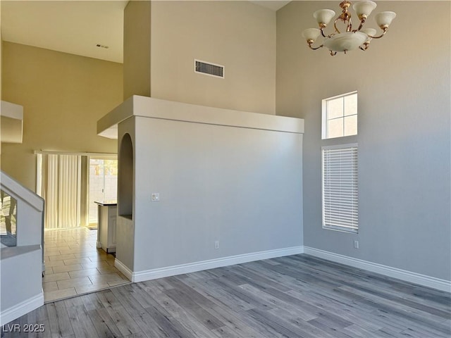 unfurnished room featuring visible vents, a towering ceiling, wood finished floors, and an inviting chandelier