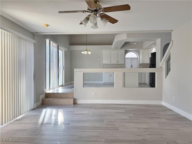 unfurnished living room with baseboards, plenty of natural light, light wood-style flooring, and ceiling fan with notable chandelier