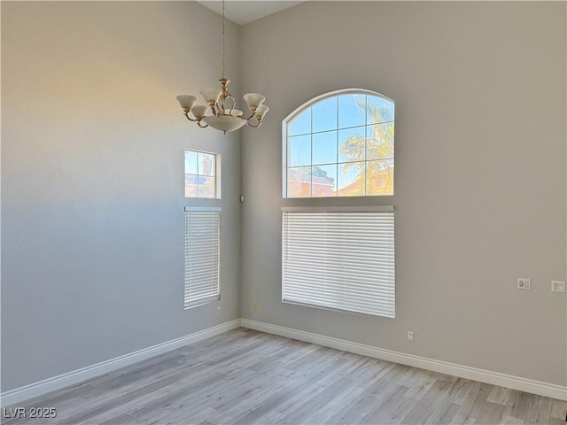 unfurnished room featuring baseboards, a notable chandelier, a healthy amount of sunlight, and light wood-style floors