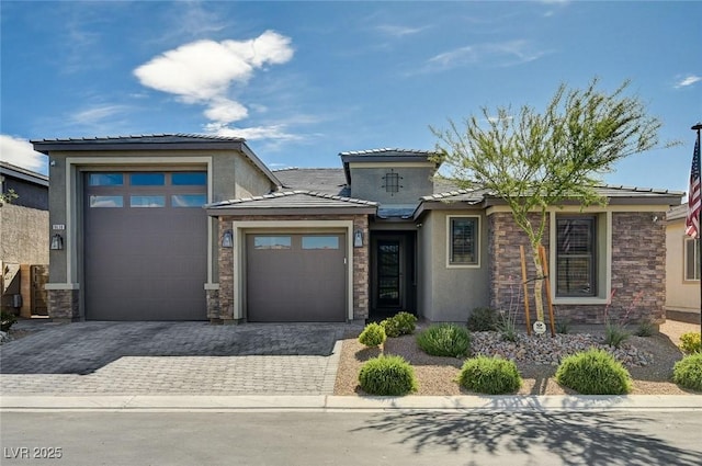 prairie-style home featuring a tiled roof, decorative driveway, an attached garage, stone siding, and stucco siding