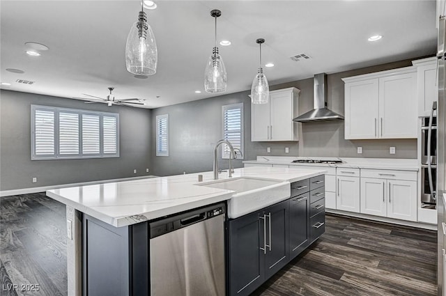 kitchen featuring white cabinets, a sink, wall chimney exhaust hood, stainless steel appliances, and visible vents