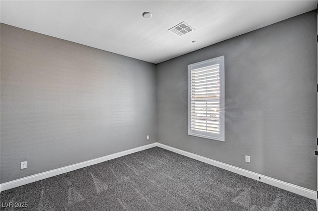spare room featuring visible vents, baseboards, and dark carpet