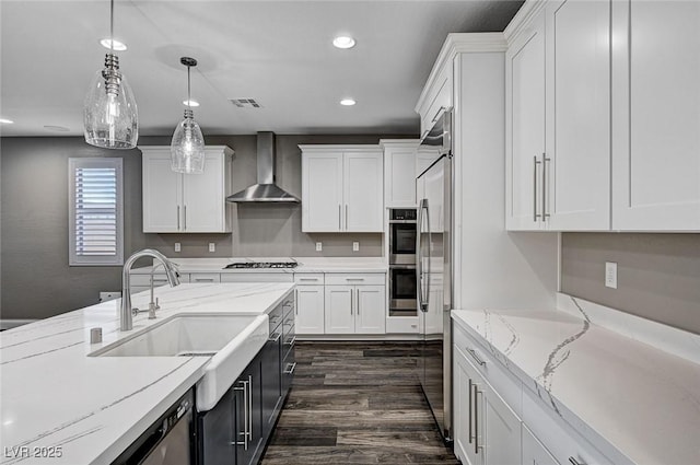 kitchen with visible vents, a sink, white cabinetry, and wall chimney range hood