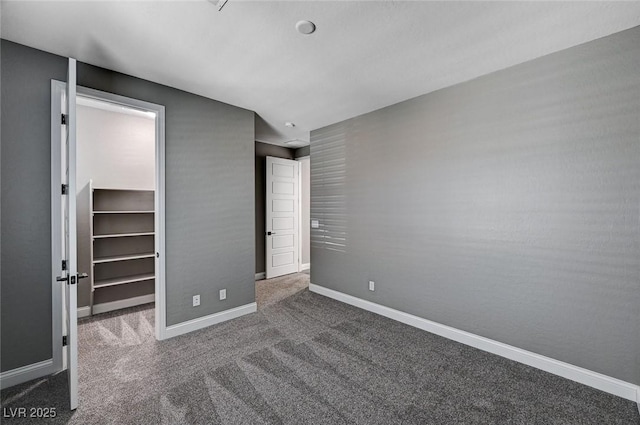 unfurnished bedroom featuring a closet, baseboards, carpet flooring, and a walk in closet
