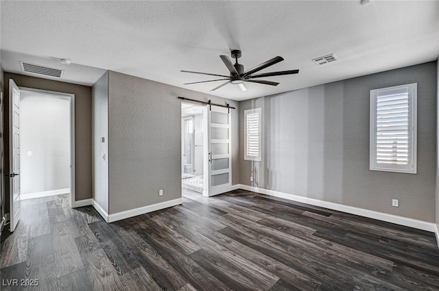 unfurnished bedroom featuring baseboards, dark wood finished floors, a barn door, and visible vents