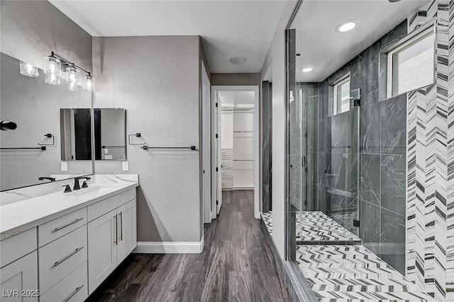 bathroom featuring a walk in closet, vanity, baseboards, wood finished floors, and a stall shower