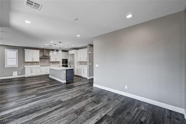 kitchen featuring visible vents, dark wood finished floors, baseboards, wall chimney exhaust hood, and an island with sink