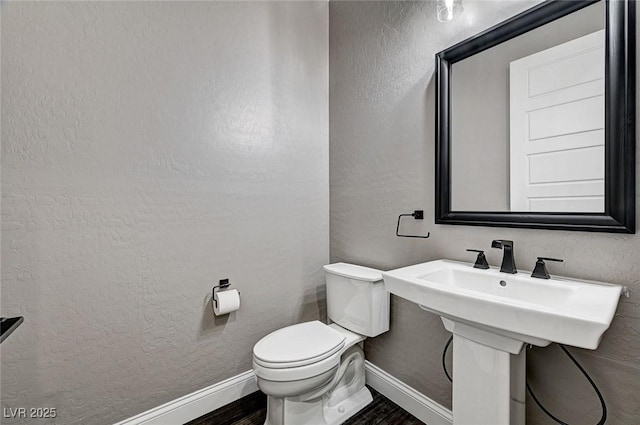 bathroom with baseboards, a textured wall, wood finished floors, and toilet