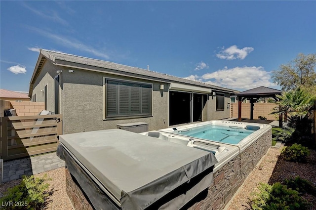 back of property featuring fence, a gazebo, a hot tub, and stucco siding