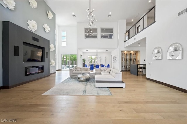 living room featuring a high ceiling, visible vents, an inviting chandelier, and light wood finished floors