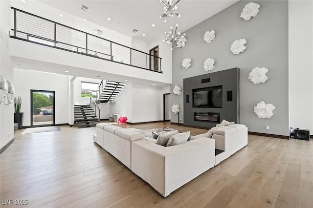living area with a high ceiling, baseboards, wood finished floors, visible vents, and stairway