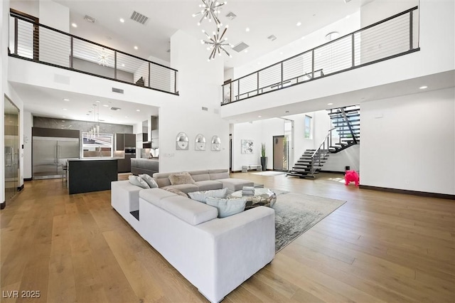 living area with a high ceiling, light wood finished floors, a chandelier, stairs, and visible vents