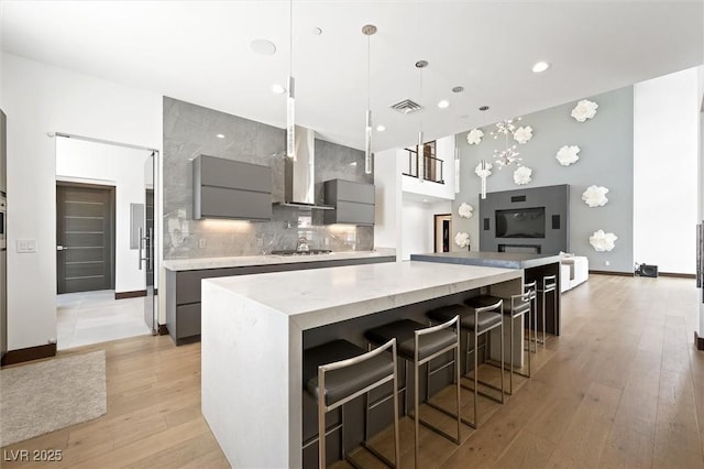 kitchen featuring gray cabinets, visible vents, modern cabinets, a spacious island, and wall chimney exhaust hood