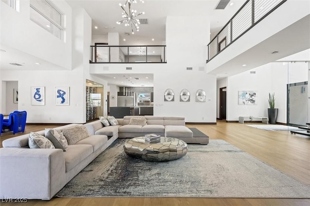 living room featuring visible vents, a towering ceiling, wood finished floors, baseboards, and a notable chandelier