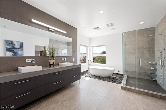 bathroom with double vanity, visible vents, a freestanding tub, a shower stall, and a sink