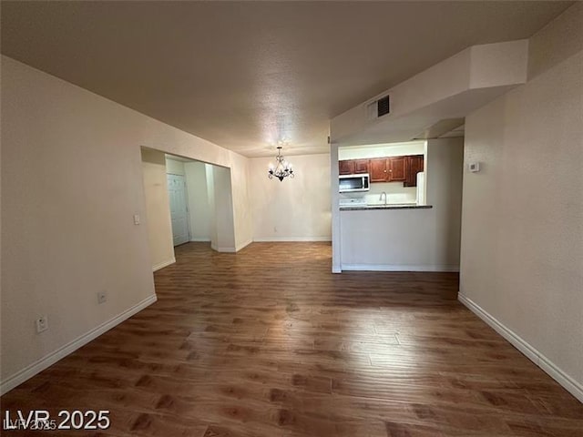 unfurnished living room with baseboards, dark wood-style flooring, a chandelier, and visible vents
