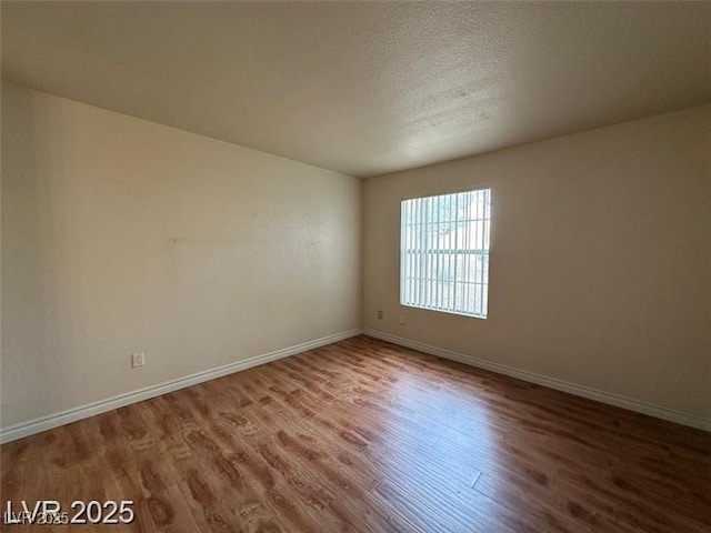 spare room featuring baseboards, a textured ceiling, and wood finished floors