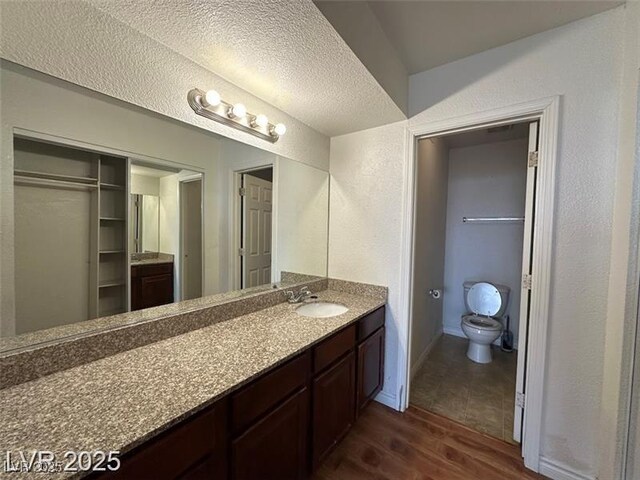 bathroom featuring a textured ceiling, wood finished floors, vanity, toilet, and a textured wall