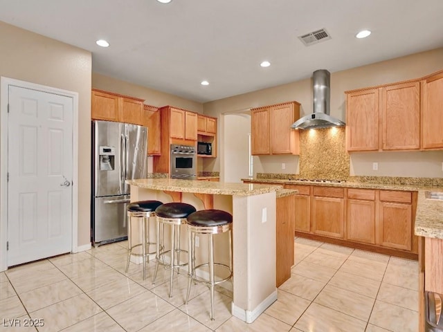 kitchen featuring light stone countertops, a breakfast bar, wall chimney range hood, a center island, and stainless steel appliances