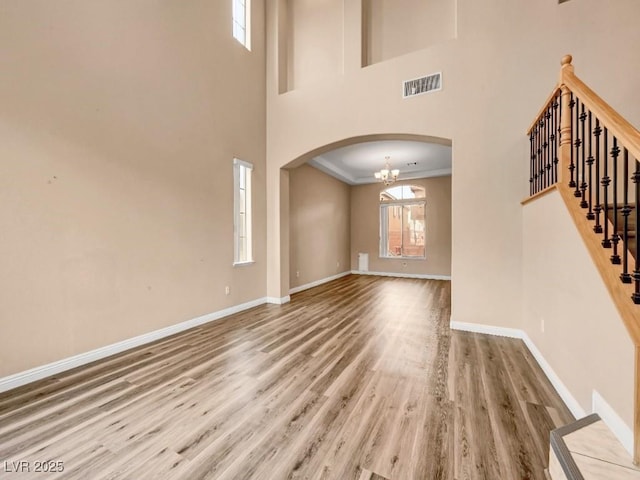 unfurnished living room with arched walkways, baseboards, visible vents, and wood finished floors
