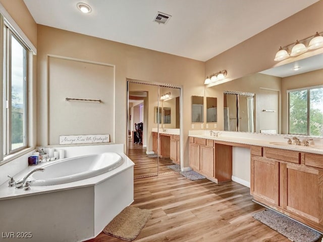 full bathroom featuring double vanity, a garden tub, visible vents, wood finished floors, and a sink