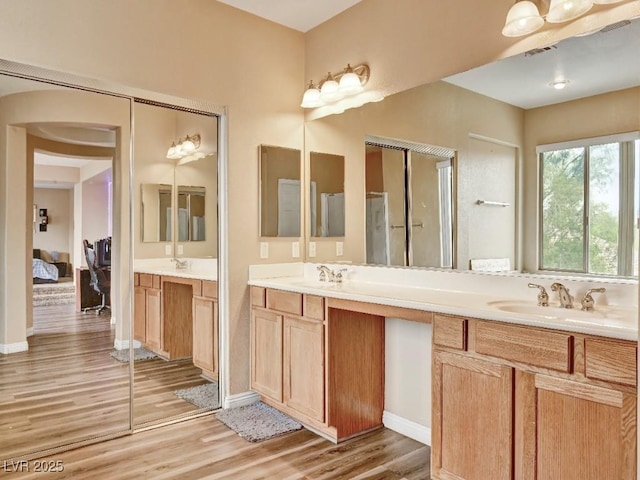 full bathroom with a sink, ensuite bath, double vanity, baseboards, and wood finished floors