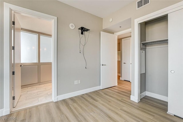 unfurnished bedroom featuring baseboards, a closet, wood finished floors, and visible vents
