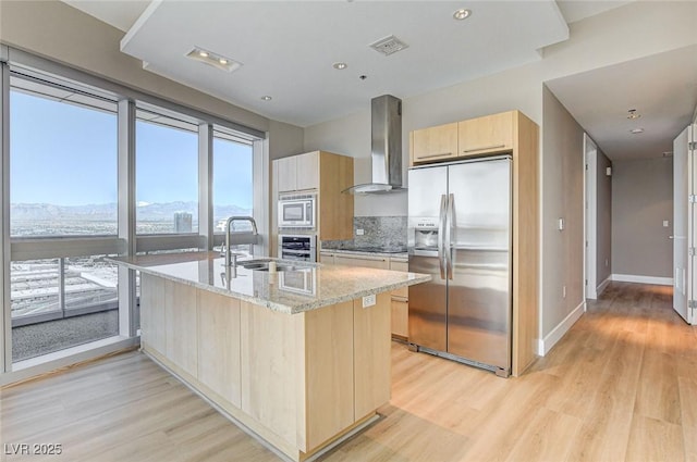 kitchen featuring light brown cabinetry, appliances with stainless steel finishes, light stone countertops, light wood-type flooring, and extractor fan