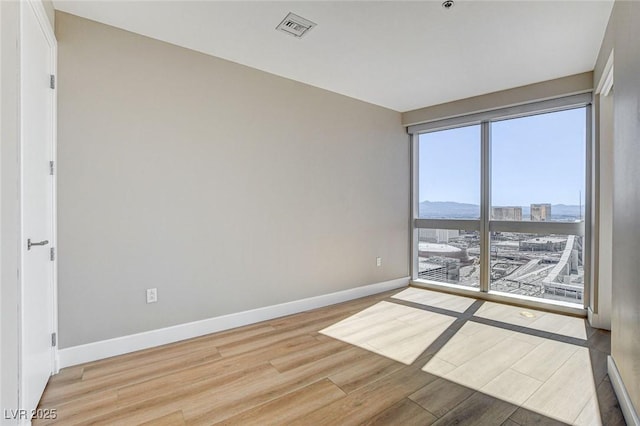 empty room featuring baseboards, a city view, wood finished floors, and visible vents