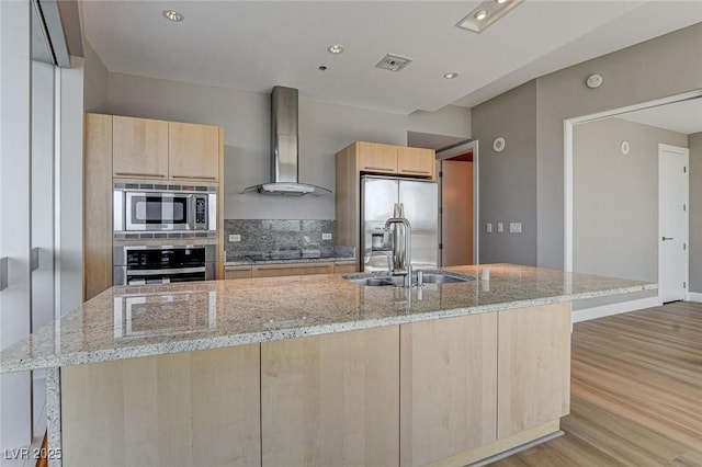 kitchen with wall chimney range hood, a sink, light wood-style floors, light brown cabinets, and stainless steel appliances