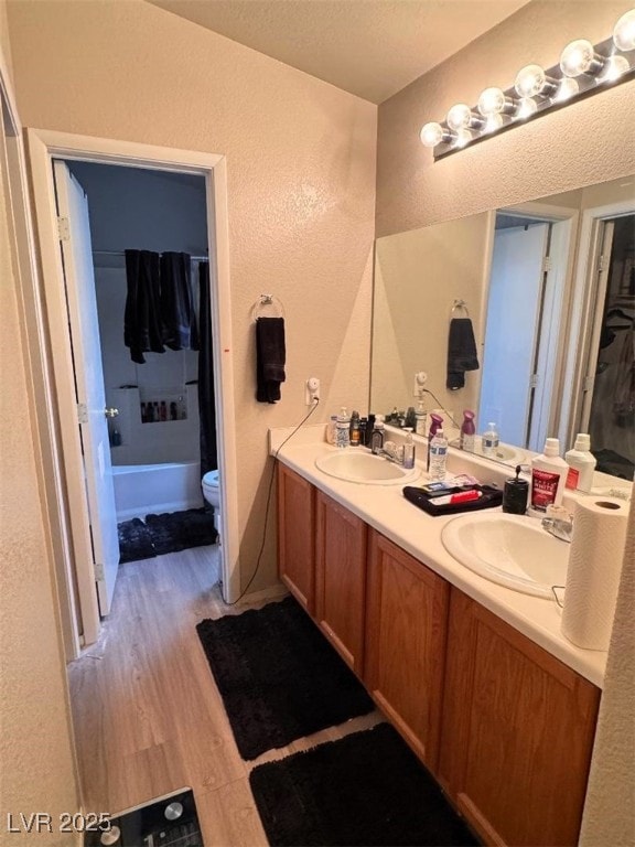 bathroom featuring double vanity, toilet, a textured wall, and a sink