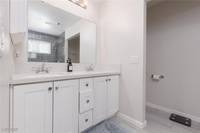full bath with double vanity, visible vents, a tile shower, a sink, and baseboards