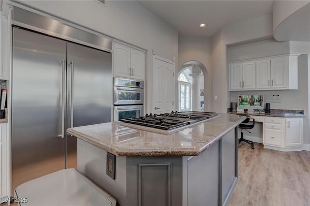 4594 Blue Mesa Way, Las Vegas, NV 89129 - kitchen featuring light stone countertops, light wood-type flooring, a center island, arched walkways, and appliances with stainless steel finishes