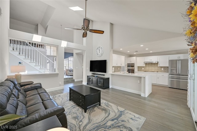living area featuring a ceiling fan, stairway, lofted ceiling, recessed lighting, and light wood-style flooring
