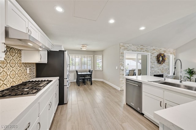 kitchen featuring backsplash, appliances with stainless steel finishes, a sink, under cabinet range hood, and white cabinetry
